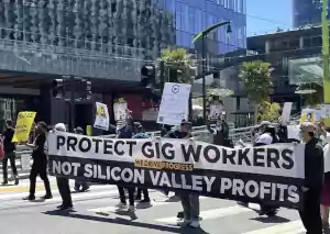 a groups of several gig workers protesting holding a banner across a crosswalk